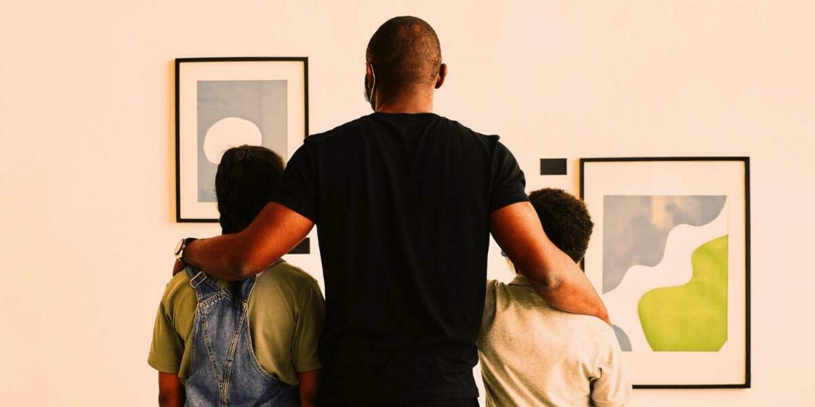 Man and two boys looking at abstract paintings on a wall