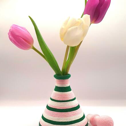 Decorative glass bottle wrapped in green, pink and cream cotton stripes of varying thicknesses.