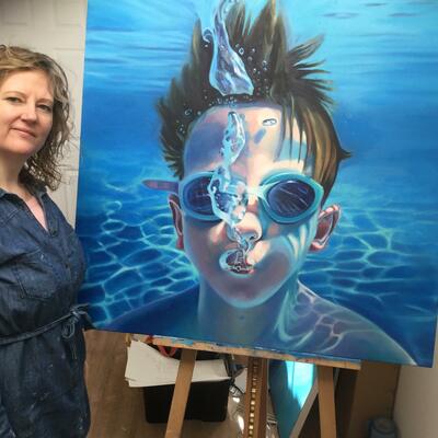 Sarah Gidden in her home studio with a large painting of a boy underwater. 