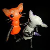 "Ginbert & Drednig" - Cotton Stitched Creatures. Hand Sewn and Painted. Part of Harts in Mind 2022 Exhibition. [Visual Description: Photo of 2 Cotton Cat-Like Creatures - One is Orange, The Other is Grey. Background is Black]