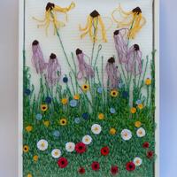 Pollinators Paradise, a tapestry woven to dipict long green grass filled with white, red, yellow and blue woven flowers and tall purple and yellow rudbeckia and echinacea flowers towering above the grass 