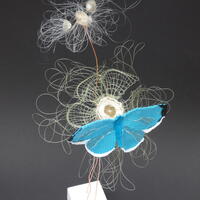 A 3D woven sculptural piece of a blue woven tapestry butterfly which is sitting on a circular woven flower under a woven fishing line seed head waiting for you to make a wish 