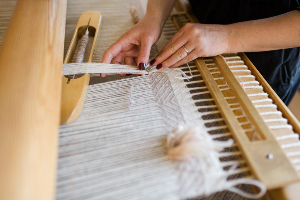 two hands weaving on a floor loom