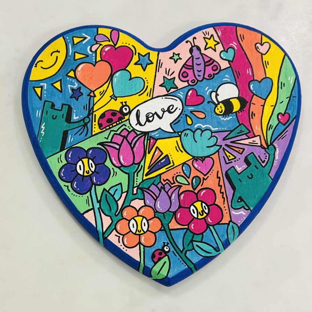 Heart shaped block of wood. Painted with very bright colours in a pop art style with the word 