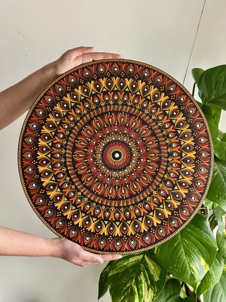 A hand-drawn mandala in vibrant colours, featuring intricate geometric patterns radiating symmetrically from a central point