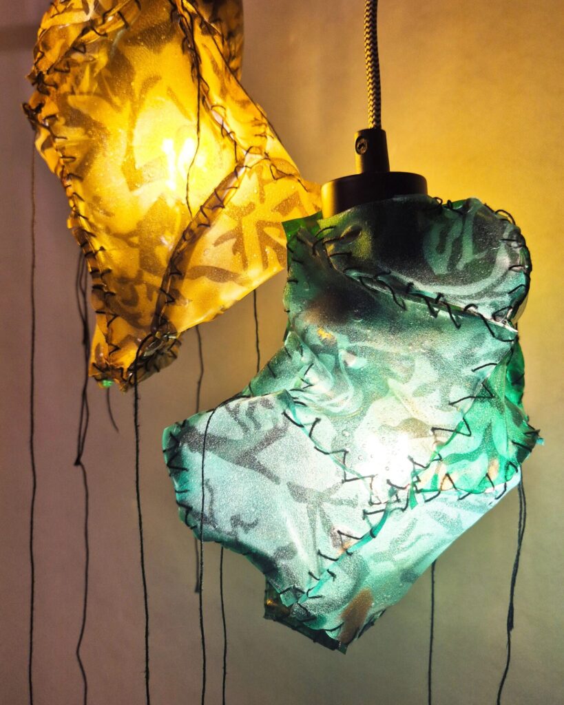Mineral by Connie Deans-Harding 2025: a stitched together angular form in translucent green material, lit from within, glyph-like marks across the surface.
